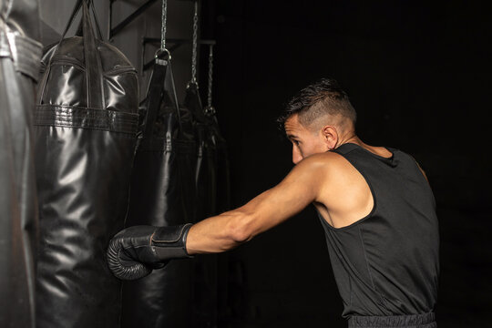 Hispanic boxer training with long heavy bag in boxing gym side view