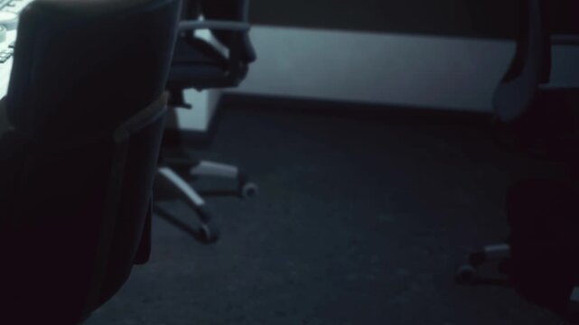 A desk is shown with an empty office chair next to it. The lighting is dim, and shadows are prominent. The scene suggests a quiet workspace after regular hours.