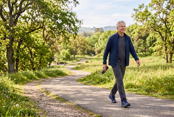 Fototapeta premium Active senior man enjoying a peaceful walk through a green park surrounded by trees, fresh scenery and natural landscapes.