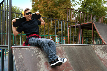 Stylish man with skateboard on ramp in skate park. Space for text © New Africa