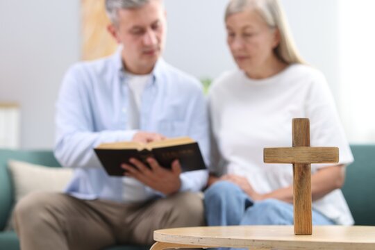 Pastor conducting Bible study with senior woman at home, focus on wooden cross