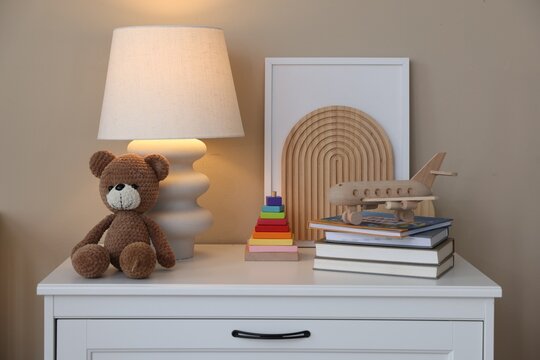 Different toys, books, lamp and other decor on cabinet in baby's room