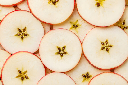 Thinly sliced red apple rounds with star cores in food background.
