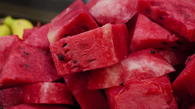 Fresh watermelon chunks cut into bite-sized pieces, showing bright red juicy flesh and black seeds in a close-up view. High quality 4k footage