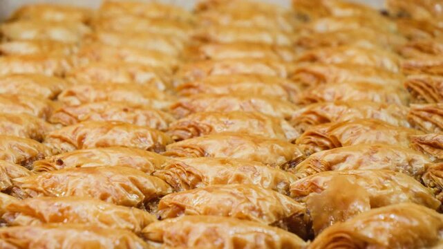 Golden baklava pastries arranged in rows, highlighting crisp layered filo dough, nut filling and glossy syrup coating in close-up. High quality 4k footage