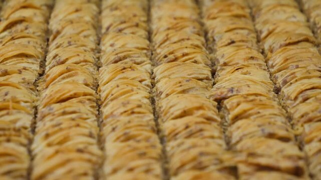 Traditional Turkish baklava pastries arranged in neat rows, showcasing layers of thin flaky pastry with a golden baked surface and syrup glaze. High quality 4k footage