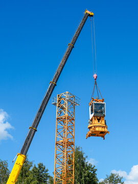 Mobile Crane Lifting Operator Cab During Tower Crane Assembly at Construction Site Under Blue Sky