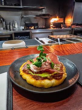 Traditional Argentine Cheese Dish: Melted Provolone (Provoleta) with Parma Ham, Chimichurri, and Microgreens Garnish on a Rustic Plate