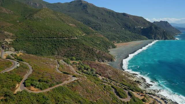 Nonza famous black sand beach aerial drone view in Cap Corse Corsica France. Scenic winding coastal road steep mountains and turquoise sea 4K stock video