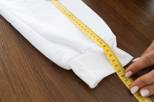 Hands measuring sleeve length on folded with yellow tape measure, highlighting precise fabric adjustment, garment fitting