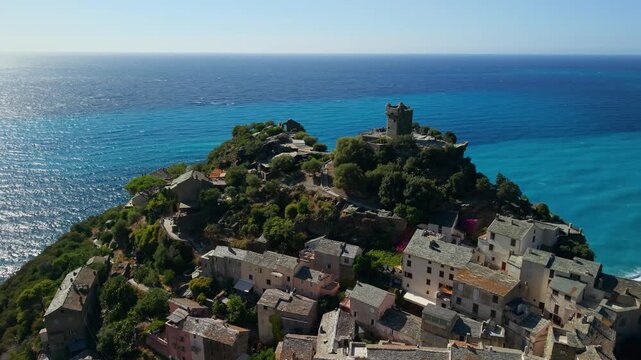 Nonza village Cap Corse Corsica 4K drone video. Half orbit around Torra di Nonza cliff tower pulling back to reveal historic old town and famous black sand beach. Scenic Mediterranean travel b roll