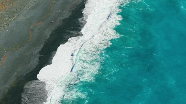 Nonza black beach aerial drone tracking shot with white wave foam on dark sand and turquoise water in Corsica. Scenic 70mm high contrast coastline 4K video
