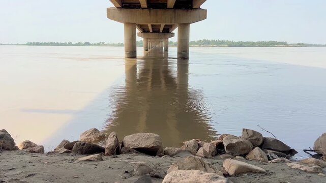view of a wide river flowing peacefully beneath a sturdy bridge in a scenic rural landscape. 4k video