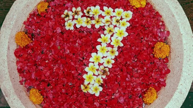 The number seven arranged from exotic flower petals, featuring delicate white frangipani blossoms against a vibrant background of red petals.