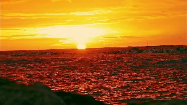The setting sun glows over the Bali Sea along the coast of Bali, casting warm golden light across the water and creating a peaceful tropical sunset scene.
