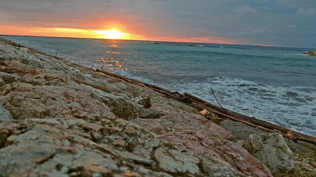 The setting sun glows over the Bali Sea along the coast of Bali, casting warm golden light across the water and creating a peaceful tropical sunset scene.