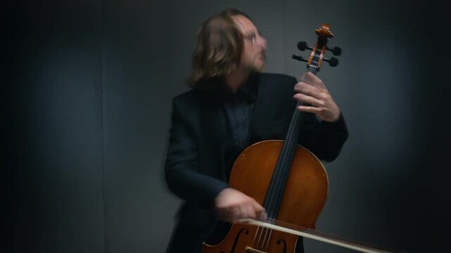 Young adult Caucasian man playing cello in studio, camera zooming out during performance. Footage is perfect for classical music marketing, concert advertisements, or artistic branding