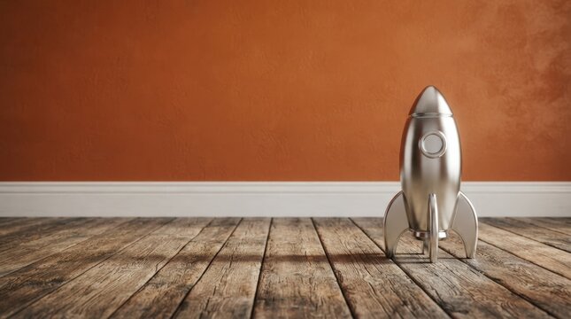 Stylish metallic rocket model on rustic wooden floor against warm orange wall ideal for creative projects, web banners, and futuristic marketing materials.