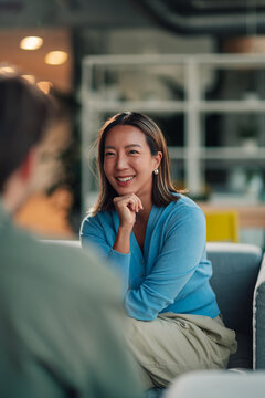 Asian businesswoman smiling while listening to a colleague, participating in a conversation, and collaborating in a modern office