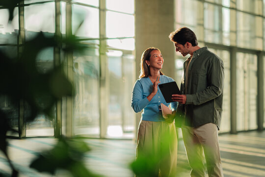 Business colleagues collaborating on a digital tablet in a modern office building, discussing project details and strategy