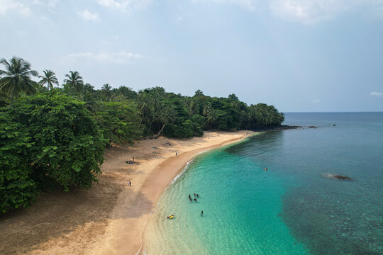 Boi beach, S&atilde;o Tom&eacute; and Pr&iacute;ncipe. Curved tropical beach with emerald-turquoise waters, dense coastal forest, and a few swimmers enjoying a secluded Atlantic bay.Africa