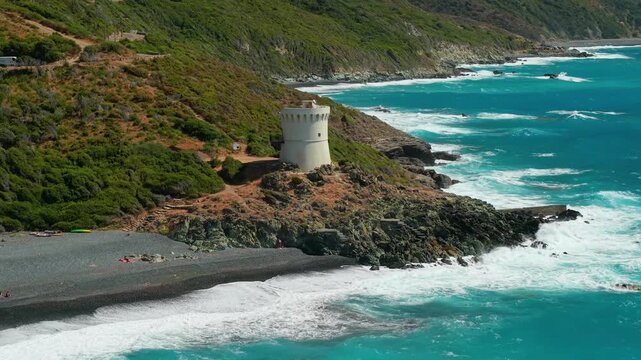 Albo beach aerial drone cinematic footage of white Genoese tower in Cap Corse Corsica. Black sand beach turquoise sea and mountains in 4K