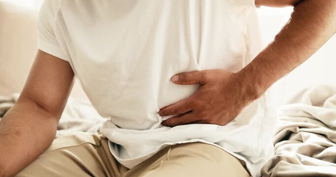 Hands, person and stomach ache in home, sick or uncomfortable with irritable bowel syndrome. Health risk, abdomen pain or man with constipation, gas bloating or diarrhea problem with food poisoning