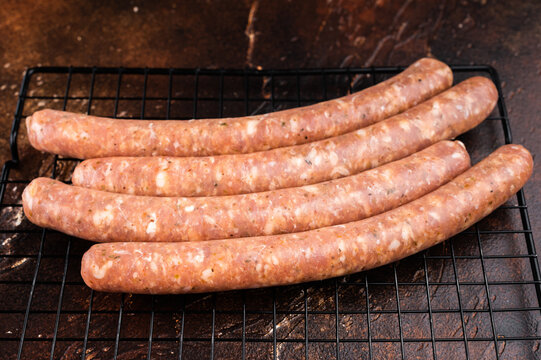 Uncooked sausage links with rosemary on metal grill rack. Fresh seasoned pork meat with coarse salt on dark textured background with copy space.