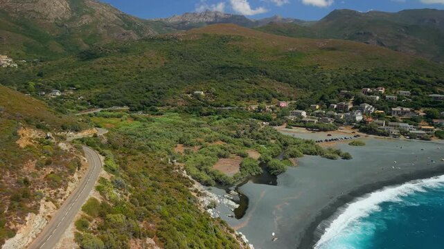 Corsica Cap Corse France 4K Aerial drone flyover from coastal road to Albo black beach with white waves and Genoese tower. Scenic tracking shot along dark sand coast and white tower rotation 