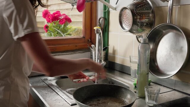 Woman performing daily routine of washing dishes by hand in a rustic home kitchen