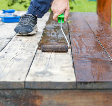Person staining wooden deck with roller