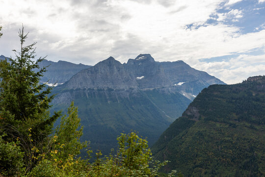 High above the road, the mountains around Logan Pass create a wild alpine panorama where rocky peaks, lingering snow, and shifting clouds meet.