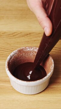 Pastry chef pipes chocolate batter into ramekin in pastry class. Pastry class teaches piping and even portions before baking. Pastry class students learn molten cake preparation and ramekin filling.
