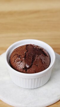Gloved hand places hot molten cake in ramekin on table. Restaurant pastry chef serves baked molten cake fresh from oven. Molten cake brings warm chocolate center to elegant fine dining dessert menu.