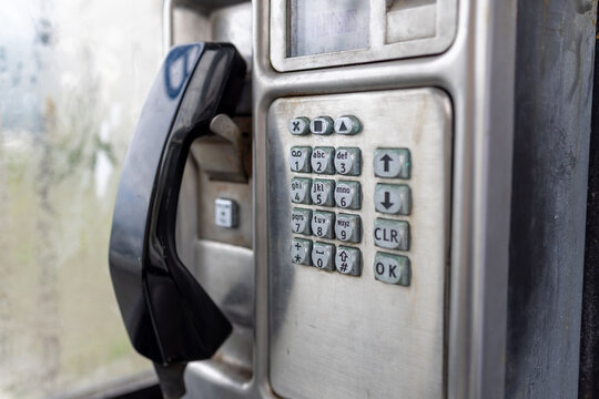Close view of an old public payphone in Llandudno North Wales showing the black handset metal keypad display and worn stainless steel casing inside a traditional telephone kiosk
