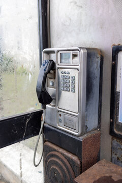 Old public payphone inside a weathered telephone kiosk in Llandudno North Wales with black handset metal keypad coin return and worn casing showing signs of age and heavy public use