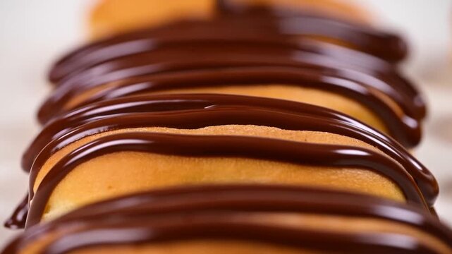 Slow motion close up of chocolate being drizzled over rows of cookies on countertop in kitchen setting