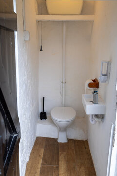 Small outside toilet at Penrhyn Bay North Wales with white walls compact hand basin toilet seat exposed pipework wooden floor toilet brush and wall mounted dispensers
