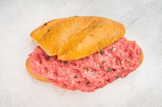 Tiger meat sandwich with seasoned raw ground beef served on bread roll on rustic cutting board