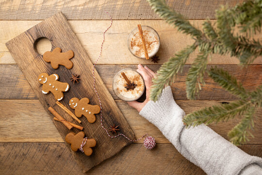 Female hand reaching for a Christmas holiday traditional eggnog across wooden table with gingerbread cookies, cinnamon sticks, star anise.