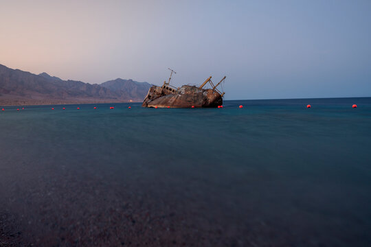 Wide shot of an abandoned rusty cargo shipwreck submerged in the calm waters of the Red Sea at twilight in Haql, Tabuk