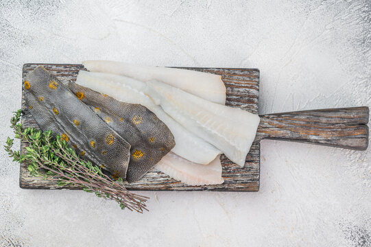 Fresh plaice flatfish fillets with herbs and garlic on wooden cutting board, raw seafood ingredient prepared for cooking on light kitchen background