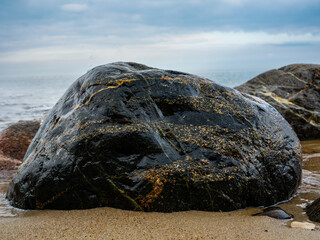 Large dark wet stone boulder on sandy beach sea background © fotomaster
