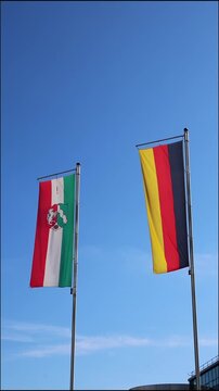 Waving flags from Germany and northrhine westphalia on blue sky background show european and german represented by German flag and northrhine westphalia flag as vertical video both flags as set