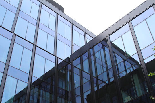 Warsaw, Poland, May 15, 2026. Low angle view of modern office skyscraper facade made of glossy dark glass panels reflecting sky. High quality photograph