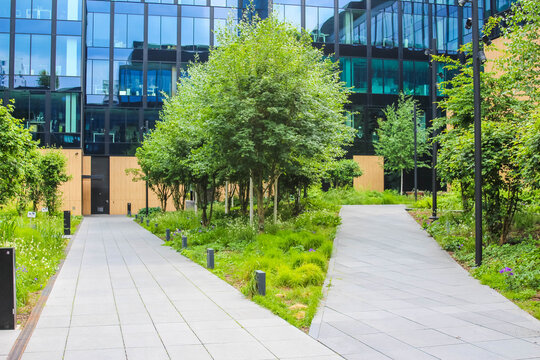 Warsaw, Poland, May 15, 2026. Forked paved pedestrian paths in modern green office park surrounded by trees and glass facades. High quality photograph