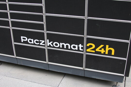 Warsaw, Poland, May 15, 2026. Yellow Paczkomat 24h signage on grey steel automated parcel delivery locker boxes outdoors. High quality photograph