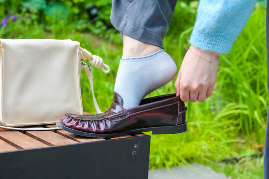 Warsaw, Poland, May 15, 2026. Close up shot of woman putting on burgundy loafer with white handbag placed on wooden surface. High quality photograph