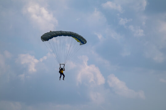 Parachutist descends through a scenic cloudy sky under a yellow and blue parachute