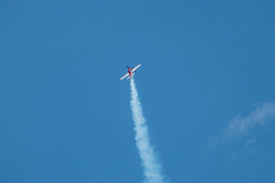 Red stunt plane ascends into a blue sky, contrails streaking behind during an aerial display